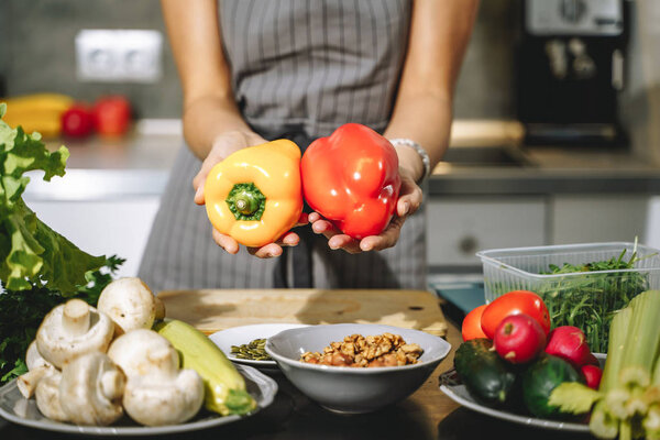 Close up of female hands holding fresh yellow and red peppers in their hands in the kitchen