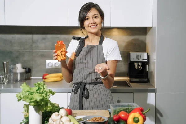 Genç ve çekici bir kadın mutfakta besin takviyeleri ya da vitaminler gösteriyor. Dengeli beslenme, sağlık ve diyet konsepti