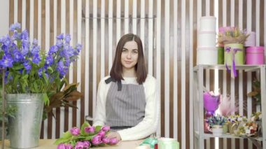 Çiçekçide ya da atölyede kameraya gülümseyen önlüklü sevimli kadın çiçekçinin yavaş çekim portresi. İnsanlar, iş ve çiçekçilik kavramı.