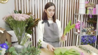 Çiçekçide ya da atölyede bir buket lale besteleyen genç kadın..