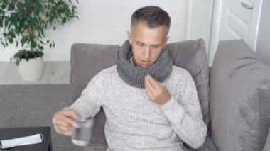 Hasta adam evdeki kanepede oturup hap alıyor.