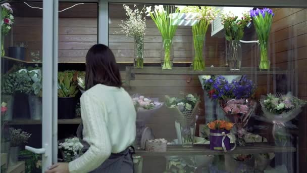 一位年轻的女花匠正在一家花店的冰箱里修理橱窗上的花束和植物 — 图库视频影像