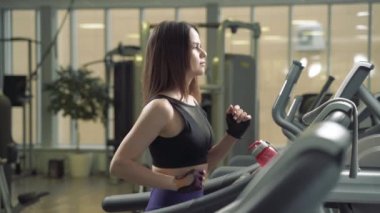 Vücut geliştiren kadın spor salonunda koşu bandında yürüyor. Spor salonunda koşu makinesi kullanan atletik bir kız..