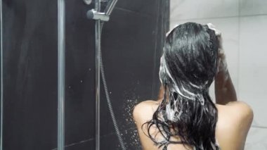Genç esmer kadın banyoda duş alıyor ve saçlarını yıkıyor. Hijyen, rahatlama ve vücut bakımı kavramı.