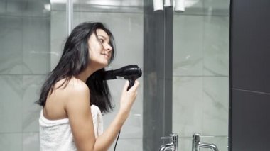 Genç bir kadın saçını bir saç kurutma makinesiyle kurutuyor ve büyük miktarda saç dökülmesinden şok oluyor.