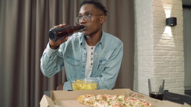 Young African Man Drinking Beer Eating Chips Watching Movie Sports — Stock Video