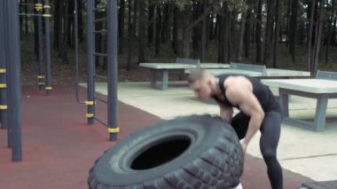 Açık havada egzersiz yaparken lastiği çeviren güçlü genç adam. Crossfit.