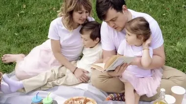 Çocuklu mutlu bir aile açık havada piknik kitabı okuyor..