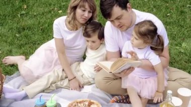 Çocuklu mutlu bir aile açık havada piknik kitabı okuyor.