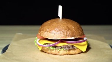 Sığır pirzolası, marul, domates ve soğanlı iştah açıcı burger. Kahverengi kağıt parçalarında servis ediliyor..