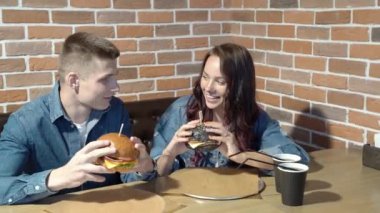 Sevgi dolu bir çift kafede konuşuyor ve hamburger yiyor.