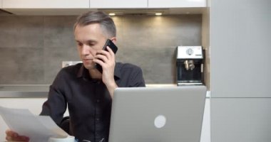 Genç adam kontrat okuyor ya da rapor yazıyor ve evde telefonla konuşuyor. Ev ofisinden bilgisayarda çalışan yakışıklı bir iş adamı.