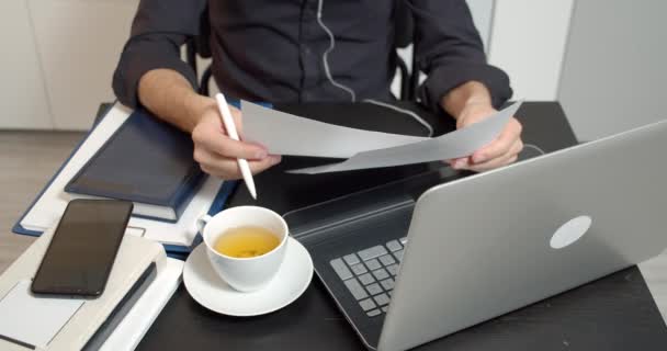 男性の手の近くに紙を保持し 契約書にメモを取るテーブルに座っている 男性起業家は書類を読み 財務書類を分析し 職場で監査報告書を作成する — ストック動画
