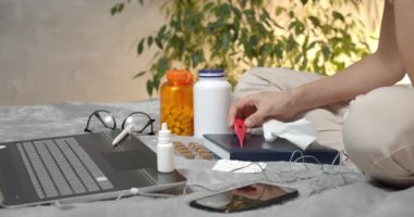 Kadın ellerinin termometreyi tuttuğu ve yatakta oturan paketten haplar aldığı yakın plan. Soğuk ya da virüs.