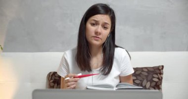 Genç hasta bir kadın termometre tutuyor. Evde bir doktora danışmak için kulaklık ve dizüstü bilgisayar kullanıyor. Teletıp ve online istişareler.