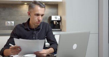 Genç iş adamı, ortaklar veya müşterilerle video bağlantısı yoluyla konuşuyor. Evde kulaklık ve dizüstü bilgisayar kullanarak bir sözleşmenin ya da yeni bir projenin şartlarını tartışıyorlar.