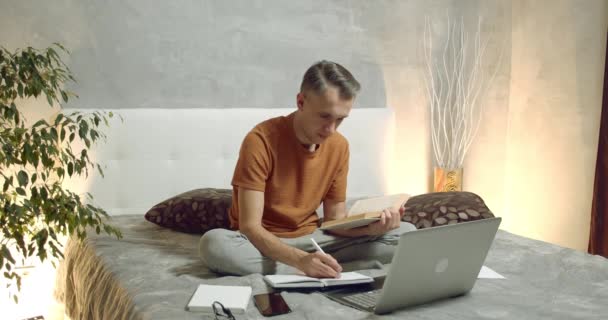 Unge Man Läser Bok Och Antecknar Laptop Som Studerar Hemma — Stockvideo