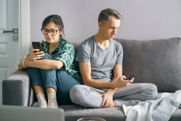 自宅のソファに座って電話を使用してソーシャルネットワークをスクロールするスマートフォン中毒のカップル インターネット中毒の概念 ロイヤリティフリーのストック写真