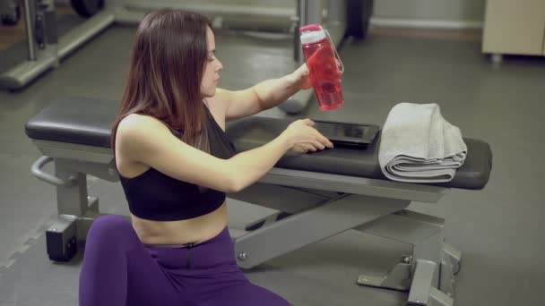フィットネスジムでのトレーニング後の休憩中に瓶から水を飲む若い女性 — ストック動画