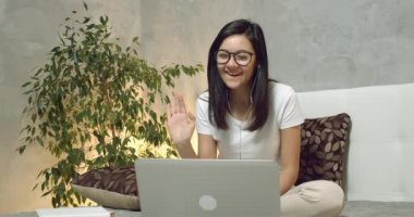 Gülümseyen genç bir kadının portresi video görüntülü konuşma yapıyor. Evinde bilgisayar ve kulaklık kullanarak web kamerasından arama yapıyor..