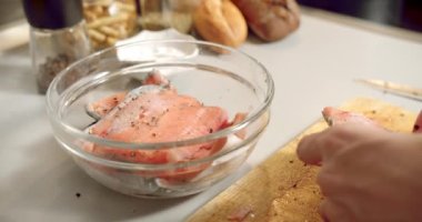 Mutfakta şeffaf bir kasede marine edilmek üzere taze somon balığı filetosu dilimleri katlayan bir aşçının kadın elleri..