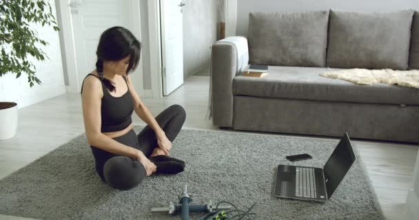 スポーティ若い女性は自宅でノートパソコンを使用してオンライン演習ストレッチを行う 健康的なライフスタイルのコンセプト 自己分離中のスポーツ — ストック動画