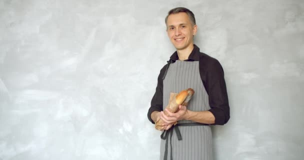 Retrato Joven Guapo Uniforme Sosteniendo Deliciosas Baguettes Frescas Sobre Fondo — Vídeo de stock