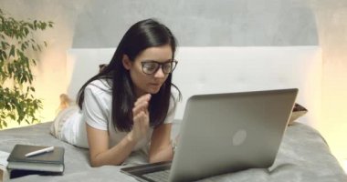 Laptop klavyesinde yazan genç bir kadın. Serbest çalışan kadın ya da öğrenci evdeki yatakta yatan sosyal ağlarda yorumlar yazıyor..