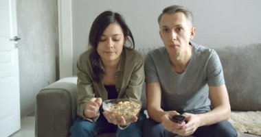 Gergin çift dikkatli bir şekilde spor maçı izliyor ya da TV 'de heyecanlı bir film izliyor ve evdeki kanepede otururken patlamış mısır yiyor..