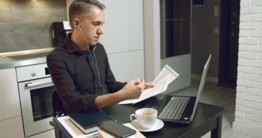 Genç iş adamı müşterilerle ya da ortaklarla görüntülü konuşma yapıyor. Evde kulaklık ve dizüstü bilgisayar kullanarak bir sözleşme veya rapor tartışıyorlar.