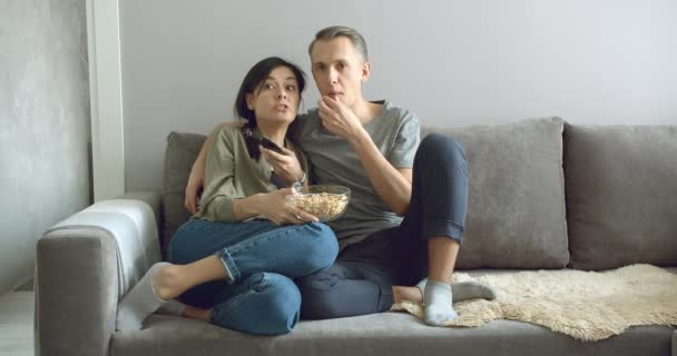 快乐的夫妻在家里坐在沙发上吃爆米花 看电视 休闲和娱乐的概念 — 图库视频影像