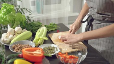 Yakın plan kadın aşçı elleri ahşap bir tahtada salata için turp doğruyor ve mutfaktaki diğer sebzelere bir kase içinde katlanıyor..