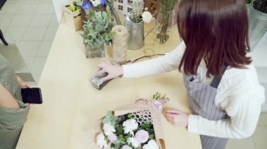 Çiçek buketi alan genç esmer kadın çiçekçide akıllı telefon kredi kartıyla NFC teknolojisiyle ödeme yapıyor. İnsanlar, alışveriş, satış, çiçekçilik ve tüketim kavramı