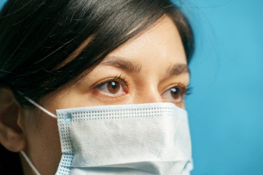 Mavi arka planda koruyucu maske takan üzgün Asyalı genç bir kadının portresi. Korku ve yalnızlık kavramı.