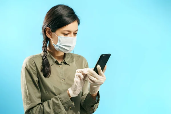 青い背景にスマートフォンを使って保護医療用マスクや手袋をした若い女性 オンラインチャット ロイヤリティフリーのストック写真