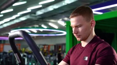 Spor giyimli genç adam eliptik makine kullanıyor ve spor salonunda kardiyo çalışması yapıyor..