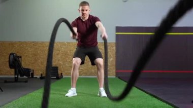 Genç kaslı adam spor salonunda ağır ip eğitimi alıyor..