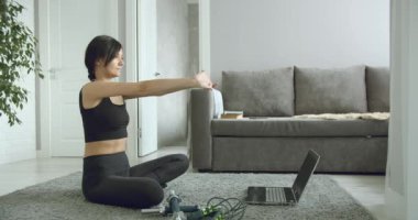 Spor yapan genç bir kadın evde dizüstü bilgisayardan spor videosu izlerken esneme egzersizleri yapıyor. Sağlıklı yaşam tarzı kavramı. İzolasyon sırasında spor.