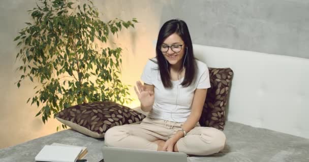 年轻微笑的女人在家里用笔记本电脑和耳机在网络摄像头上进行视频通话的肖像 — 图库视频影像