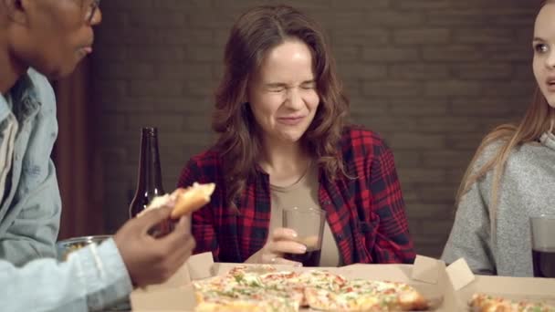 若い白人女性は 彼らがピザを食べているときに友人との会議で面白い冗談で笑って 自宅やバーで一緒にビールを飲んでいます — ストック動画