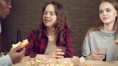 Bir grup mutlu çoklu etnik arkadaş evde ya da barda bira içip pizza yerken komik bir fıkraya gülüyorlar..