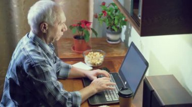 Akşamları evde dizüstü bilgisayarla çalışan yaşlı bir adam klavyede daktilo çalıyor..