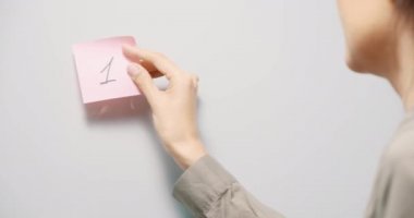 Gri tahtaya üzerinde 113 numara yazan pembe hatırlatıcı çıkartmalar yapıştıran genç bir kadın. Boşluğu kopyala.