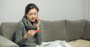 Vücut ısısını ölçen hasta bir genç kadının portresi ve evdeki kanepede otururken konsültasyon için doktor çağırması..