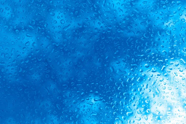Grandes gotas de agua en el vaso. Gotas de lluvia sobre el vidrio sobre el fondo del cielo azul. Copiar espacio. Color de moda 2020. Fondo azul clásico . — Foto de Stock