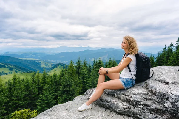 Een jong meisje staat bovenop een berg in bewolkt weer genieten van het uitzicht — Stockfoto