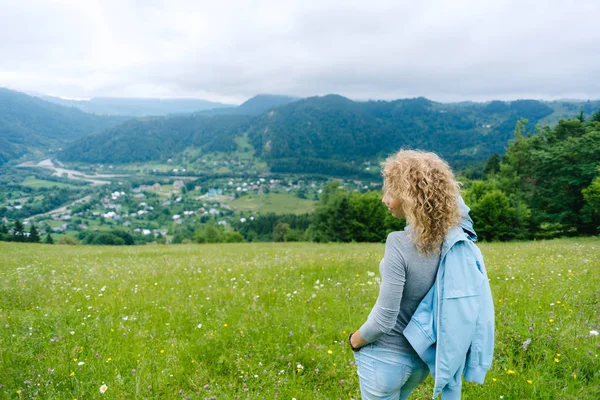 Een jong meisje staat bovenop een berg in bewolkt weer genieten van het uitzicht — Stockfoto