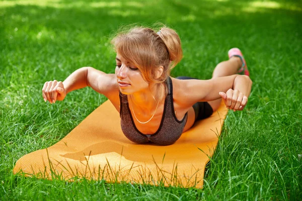 Meisje doet oefeningen op de mat in het park op het groene gras Stockafbeelding