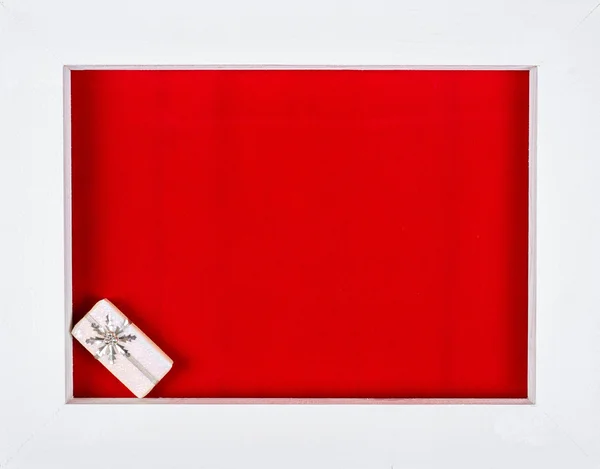 Beyaz ahşap çerçeve ve kırmızı bir arka plan üzerinde bir Noel hediyesi — Stok fotoğraf