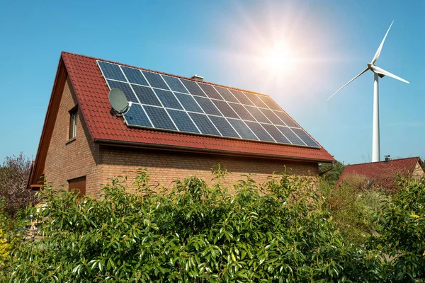 Painel solar em um telhado de uma casa e turbinas eólicas arround - conceito de recursos sustentáveis — Fotografia de Stock